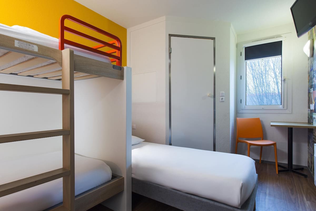 A bunk bed room with a desk and chair, a door, and a window with a view.