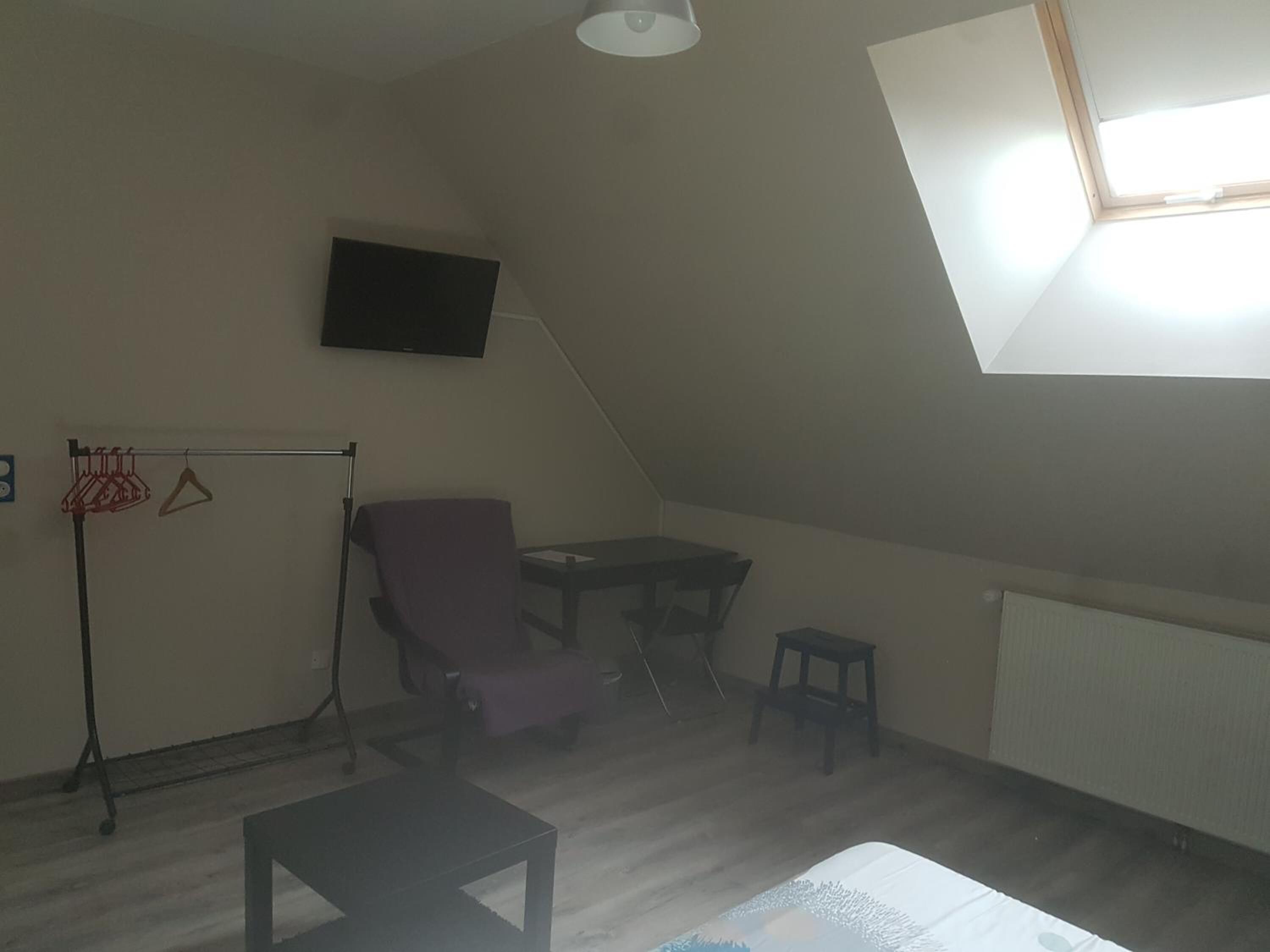Une pièce avec un plafond en pente, un téléviseur fixé au mur, une chaise, une petite table et un panier de basket.