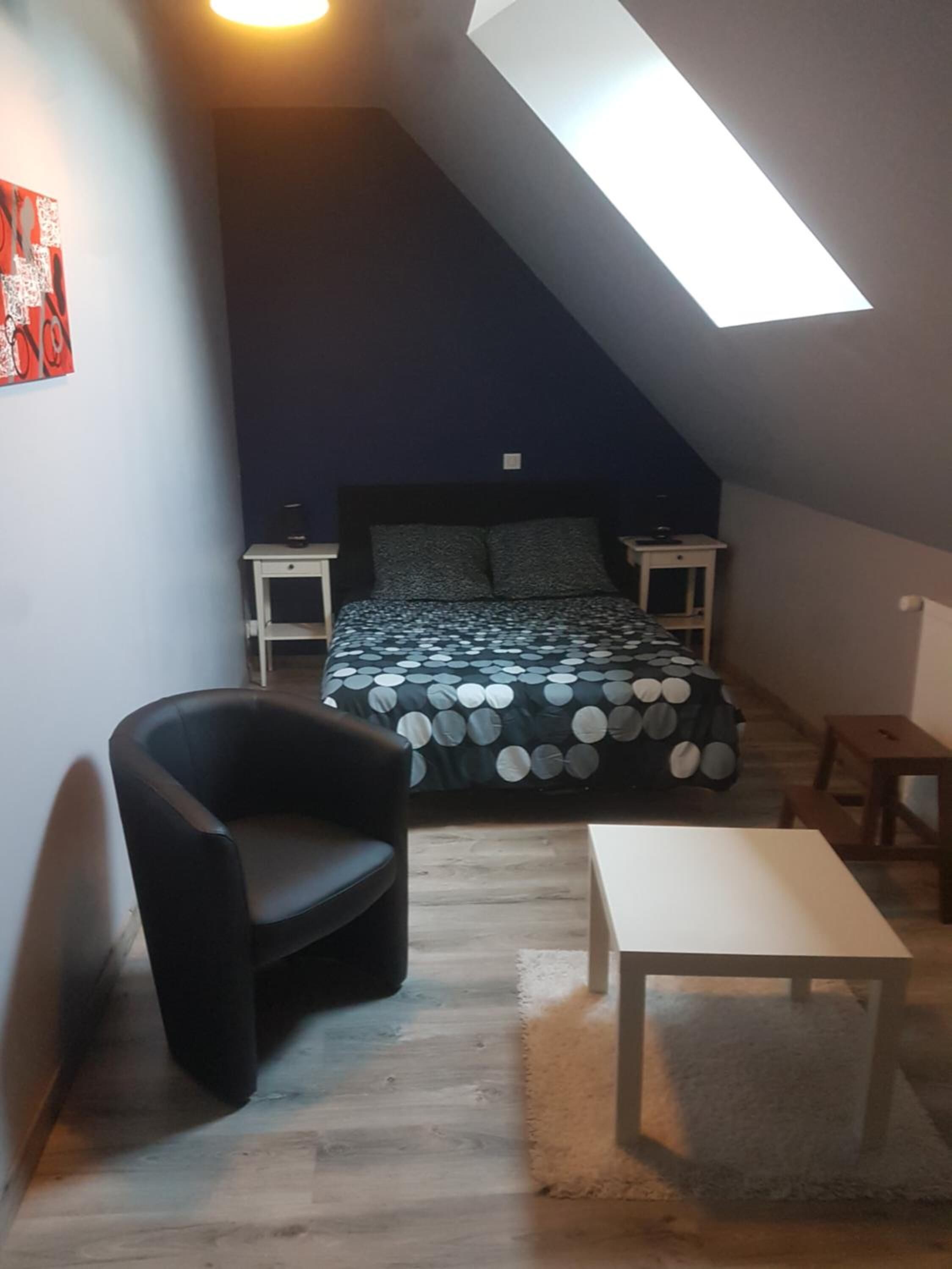 A small, cozy room with a bed, a chair, a table, and a skylight.