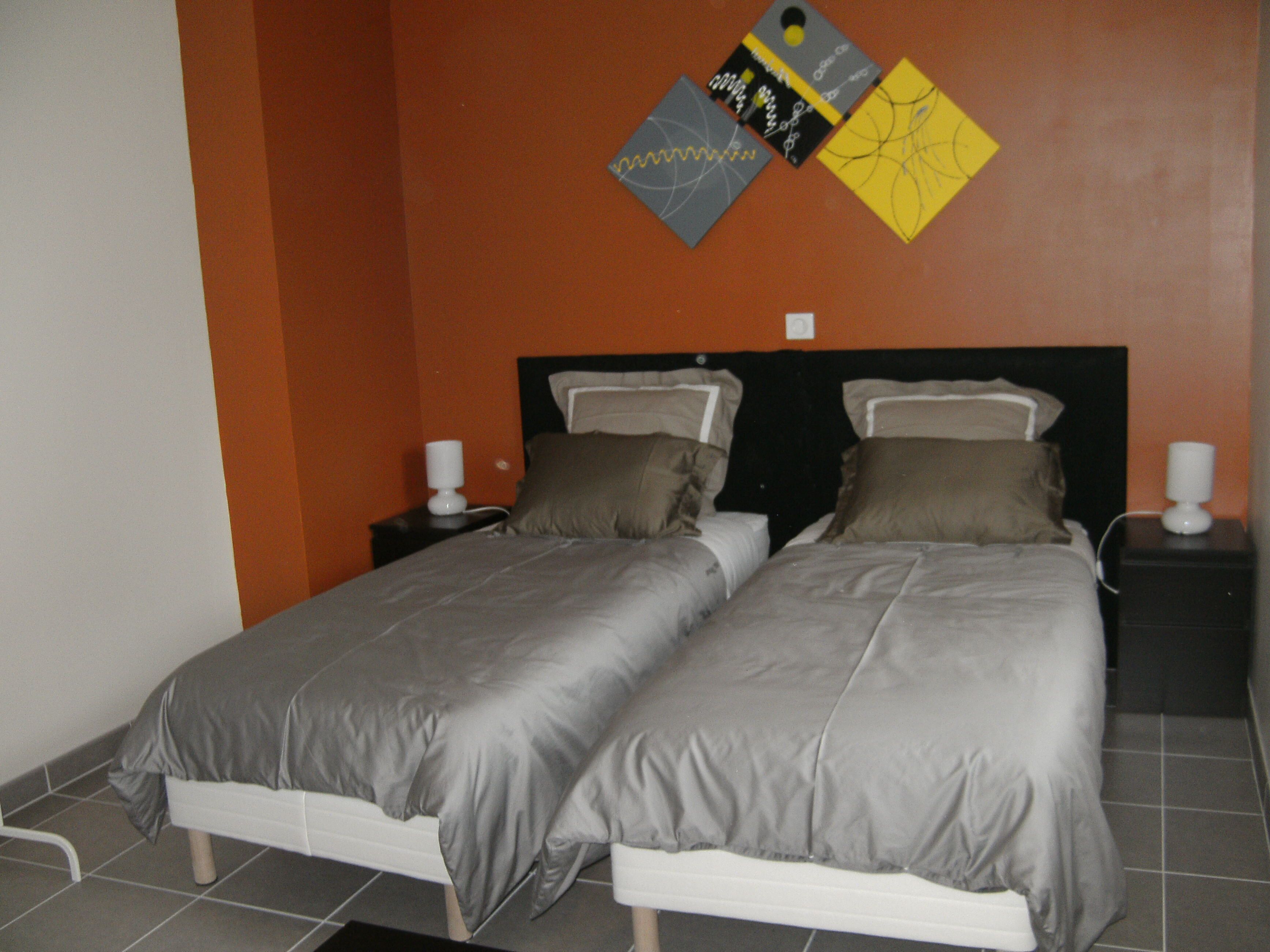 A double bed with grey bedding, two bedside tables with lamps, and a wall with abstract art.