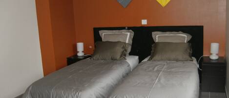 A double bed with grey bedding, two bedside tables with lamps, and a wall with abstract art.
