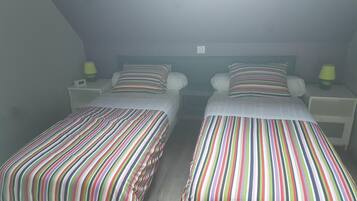 A twin room with two single beds, each with striped bedding, bedside tables with lamps, and a small window.