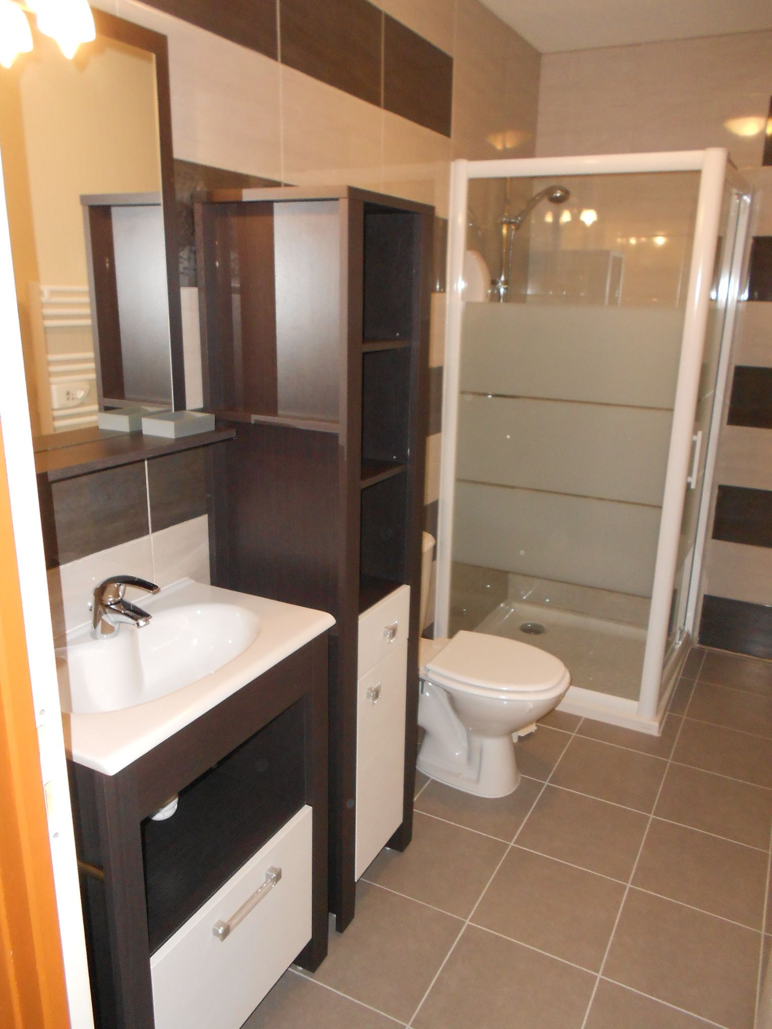 A bathroom with a sink, mirror, cabinet, toilet, and glass-enclosed shower.
