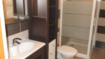 A bathroom with a sink, mirror, cabinet, toilet, and glass-enclosed shower.