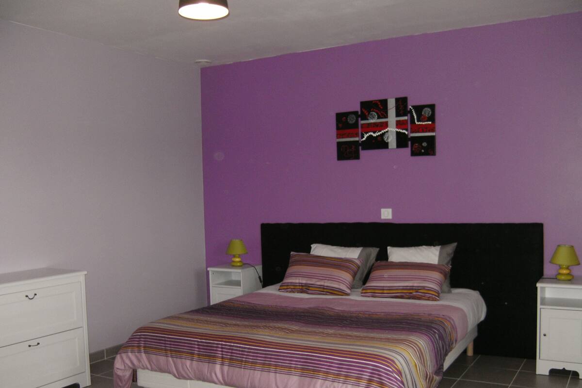 A bedroom with a bed, two bedside tables, a nightstand, a dresser, and a wall with a decorative piece.