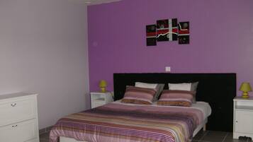 A bedroom with a bed, two bedside tables, a nightstand, a dresser, and a wall with a decorative piece.