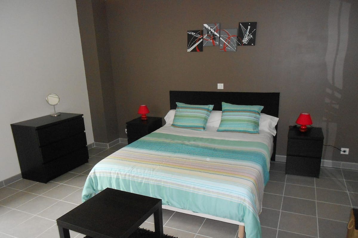 A bedroom with a bed, two bedside tables, a nightstand, a small table, and a mirror.