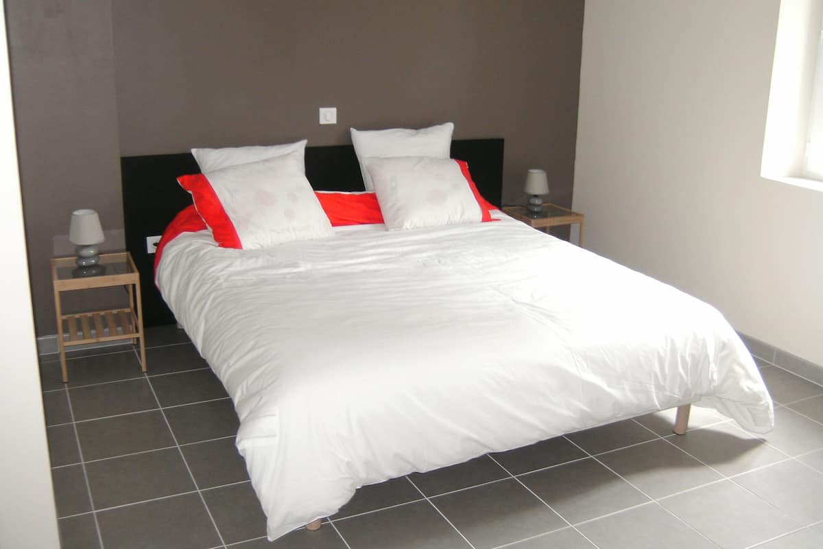 A neatly made bed with white and red bedding, two bedside tables with lamps, and a plain wall.