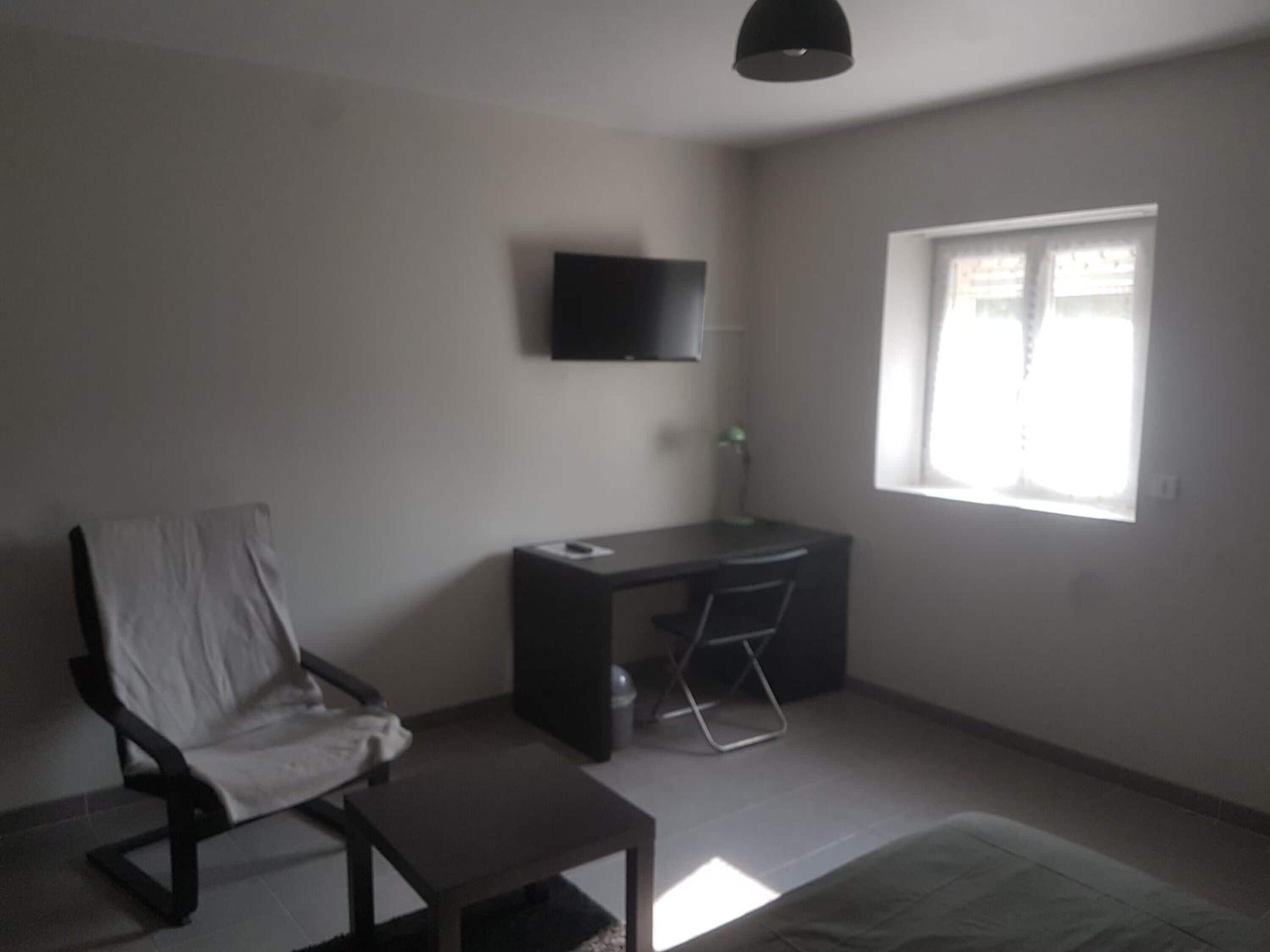 A small, sparsely furnished room with a desk, chair, and a television mounted on the wall.