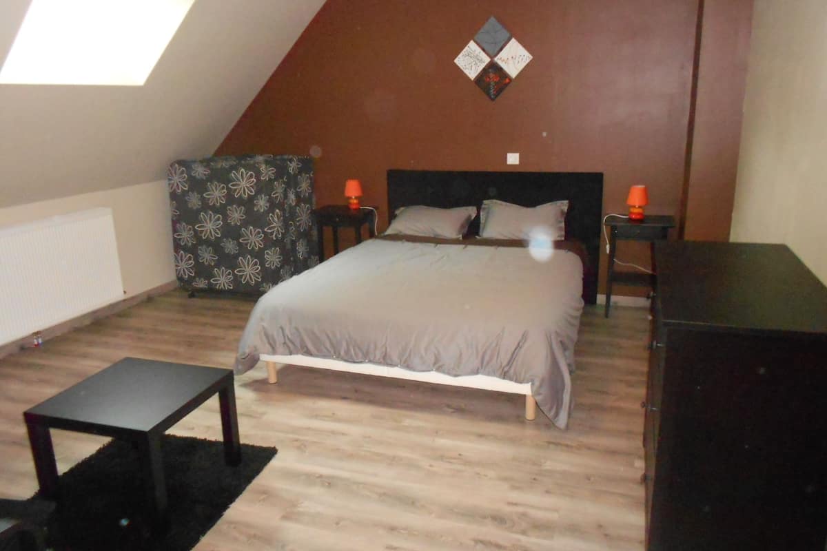 A bedroom with a bed, two nightstands, a dresser, a small table, and a patterned chair.