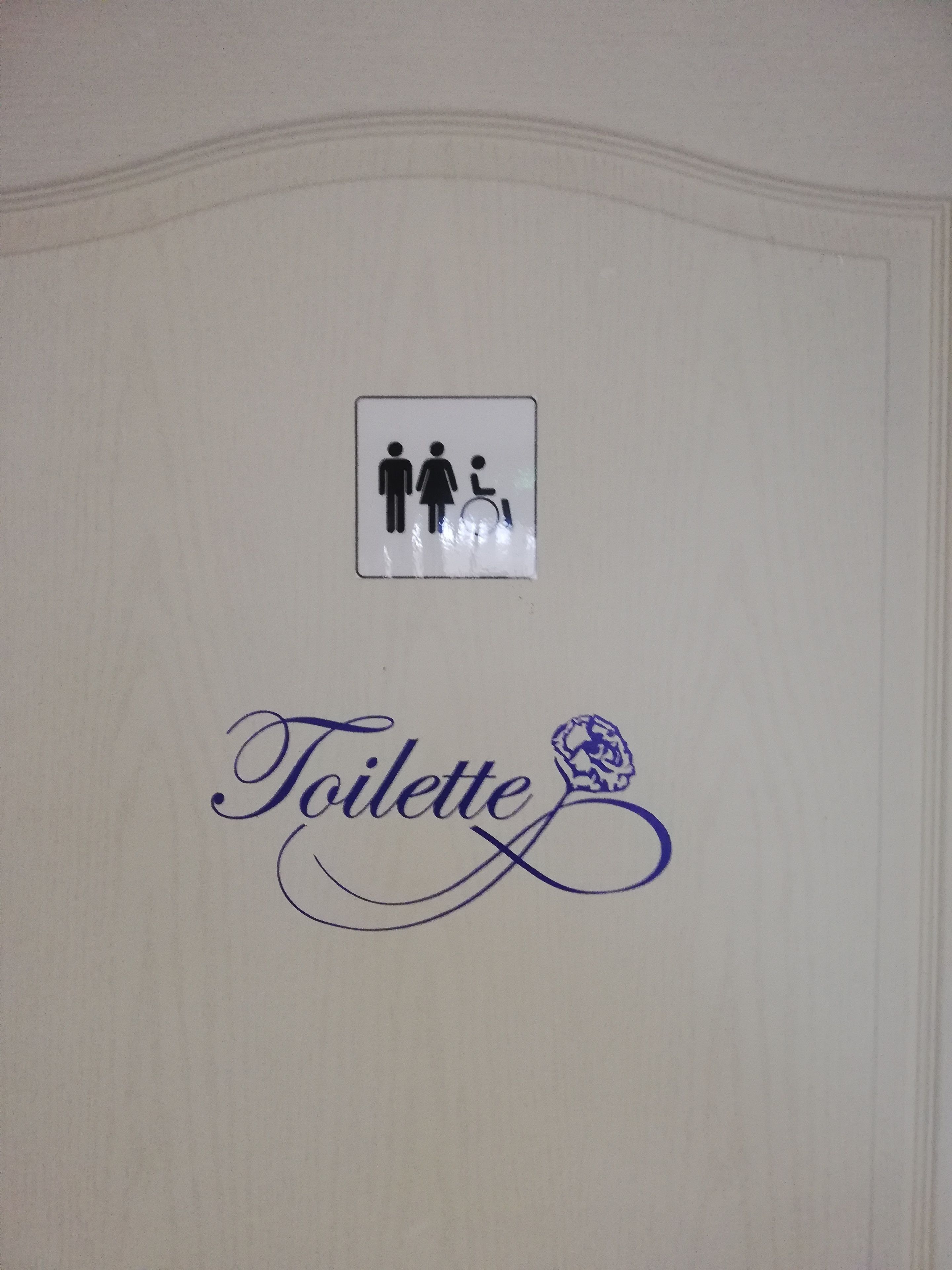 Señal de baño con el símbolo de accesibilidad para sillas de ruedas y la palabra 'Toilette' en una tipografía estilizada.