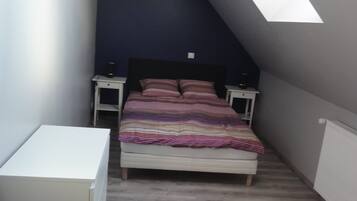 Een slaapkamer met een schuine kap, een bed met een gestreept dekbedovertrek, nachtkastjes en een klein witte tafeltje.