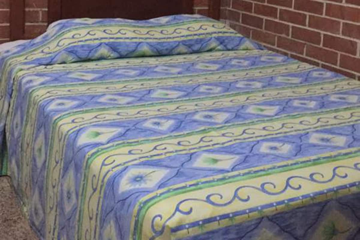 A room with two beds, each with a patterned bedspread. The room has brick walls and a wooden headboard.