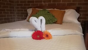 A bed with a quilted white cover, a brick wall, and a green patterned pillow. - Hotel Villa Los Arcos (Flores)