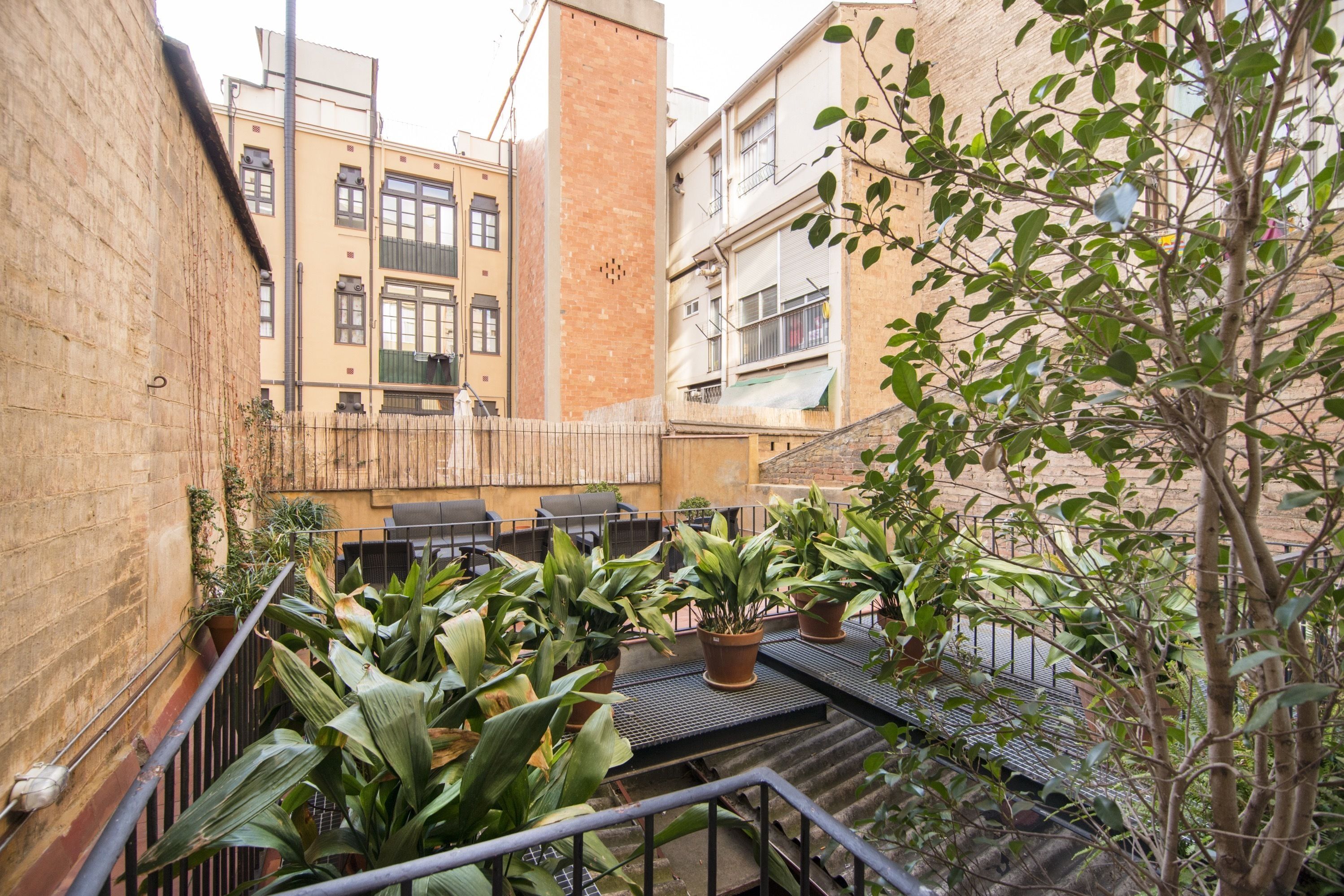 A courtyard with potted plants, outdoor seating, and a staircase leading to an upper level.