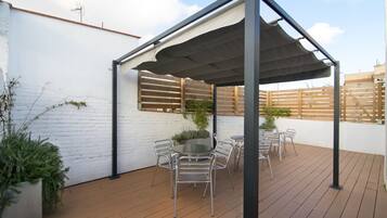 Een overdekt terras met een houten terras, metalen stoelen en een tafel.