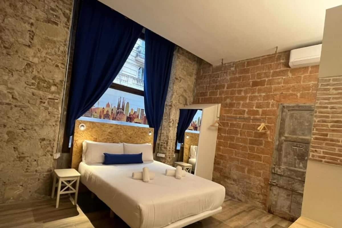 Um quarto com uma cama grande, uma mesinha de cabeceira, um espelho e uma parede de tijolos.