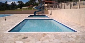 A swimming pool with a stone deck and a slide. - Pousada Rural Águas da Prata (Aguas da Prata)