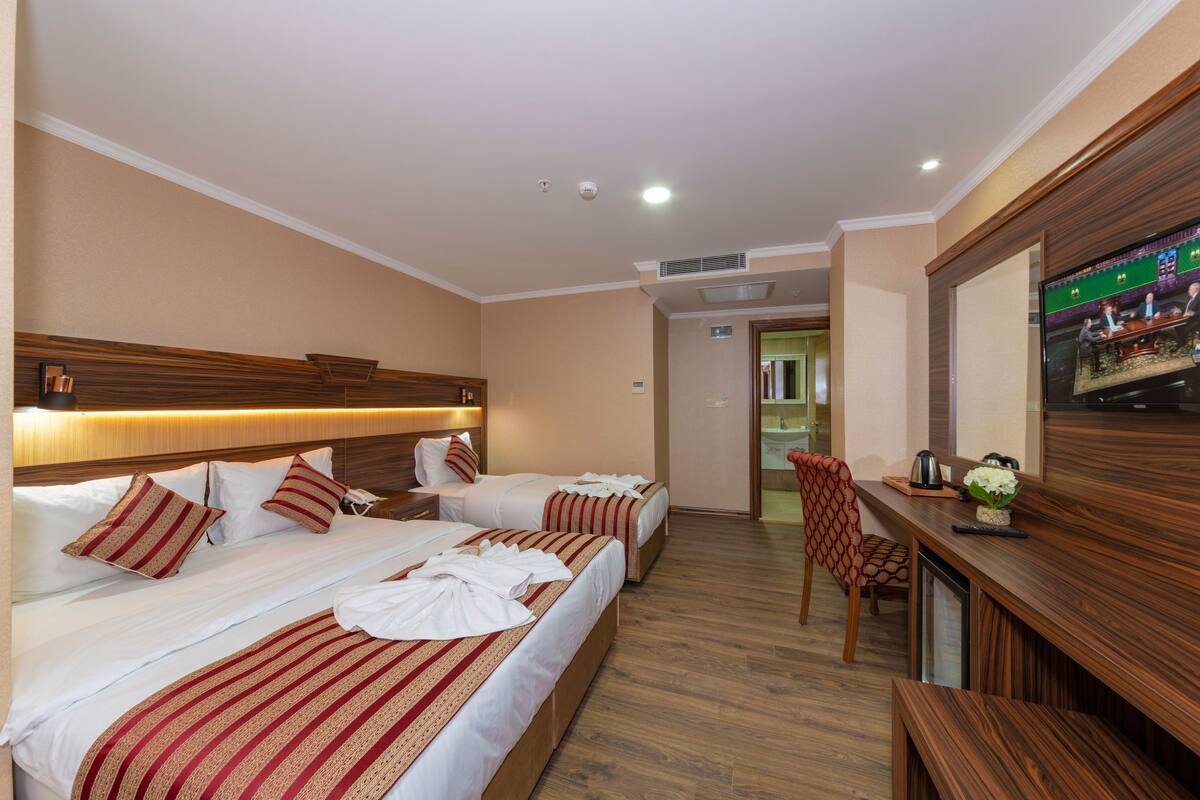 Une chambre d’hôtel avec deux lits, une tête de lit en bois, un bureau avec une télévision et une chaise.