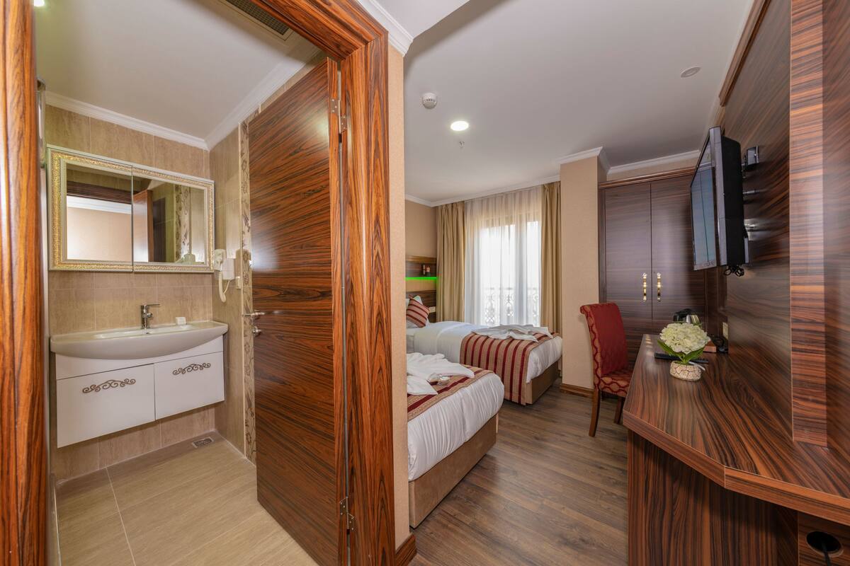 Une chambre d’hôtel avec une armoire en bois, un lit avec une literie blanche, une chaise rouge, un bureau en bois et un téléviseur.