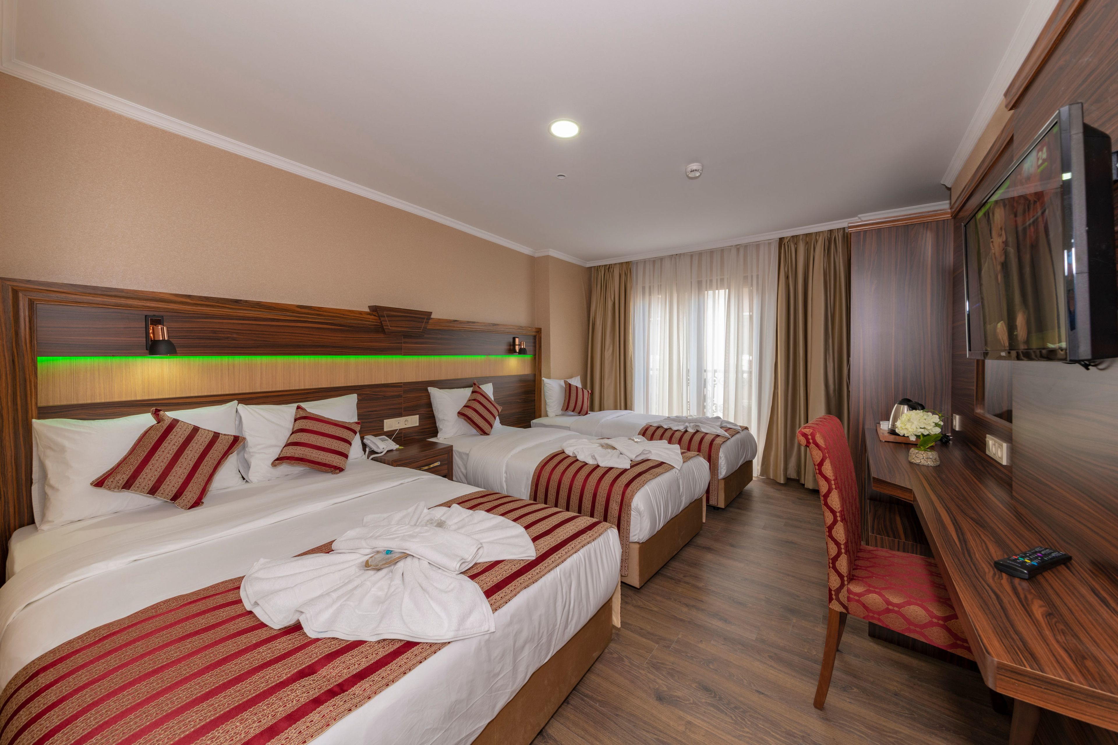 A hotel room with three beds, a desk, a chair, and a TV.