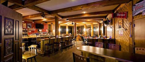 Un rincón acogedor de bar con vigas de madera, taburetes y una barra.