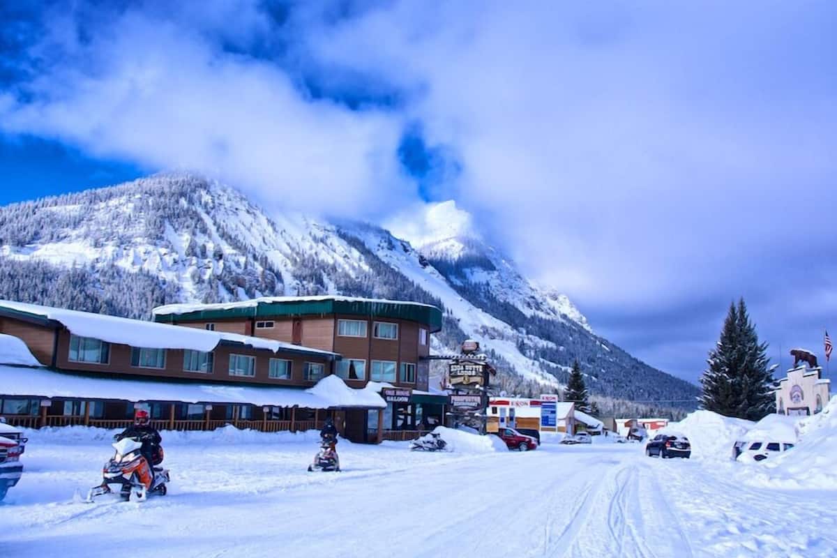 Une ville de montagne enneigée, avec un centre de sports d’hiver, un espace de location de motoneiges et un paysage montagneux en toile de fond.