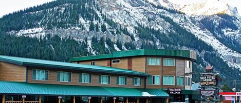 A lodge with a green roof and wooden facade, surrounded by snow-covered mountains.