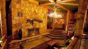 A cozy interior with a stone fireplace, wooden furniture, and a staircase leading to an upper level. - Soda Butte Lodge (Cooke City)