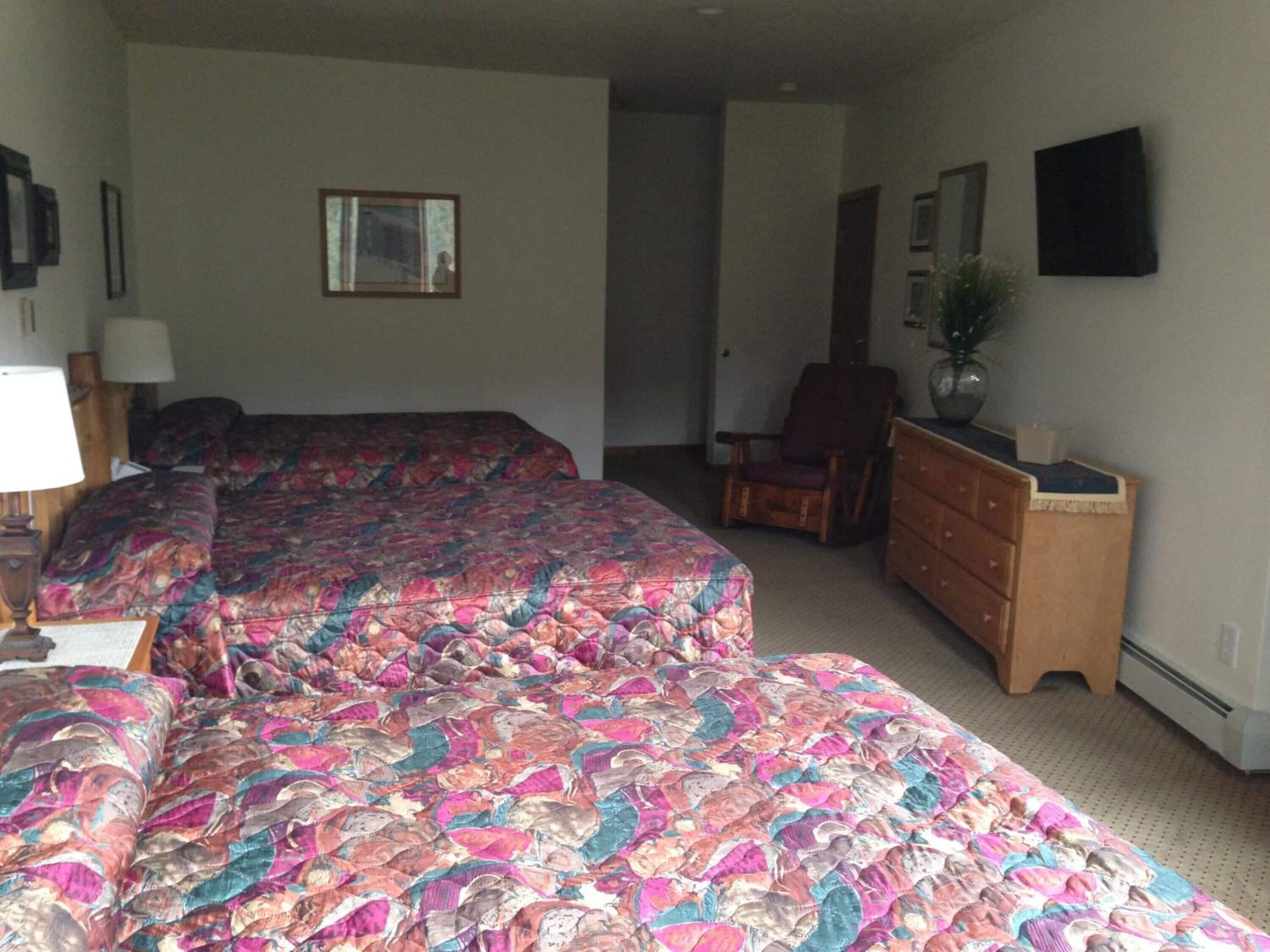 Ein Hotelzimmer mit zwei Betten, einem Schminktisch, einem Sessel und einem Fernseher an der Wand.