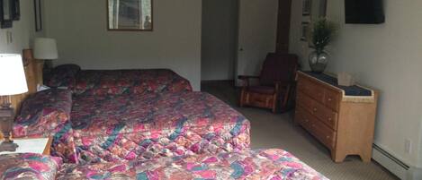 A hotel room with two beds, a dresser, a chair, and a television on the wall.