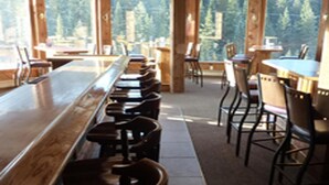A restaurant with a long counter and multiple tables and chairs. - Soda Butte Lodge (Cooke City)