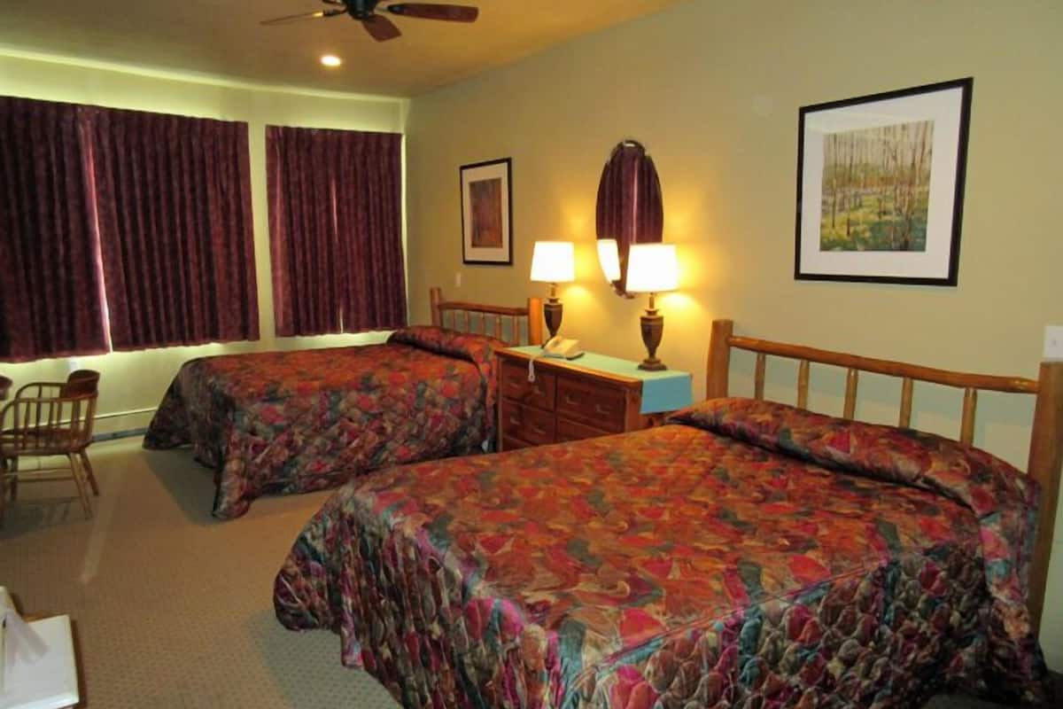 Une chambre d’hôtel avec deux lits, un bureau avec une lampe, une chaise et un ventilateur de plafond.