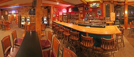 Uma área de bar com diversas opções de assento, incluindo banquetas e mesas, e uma mesa de bilhar.