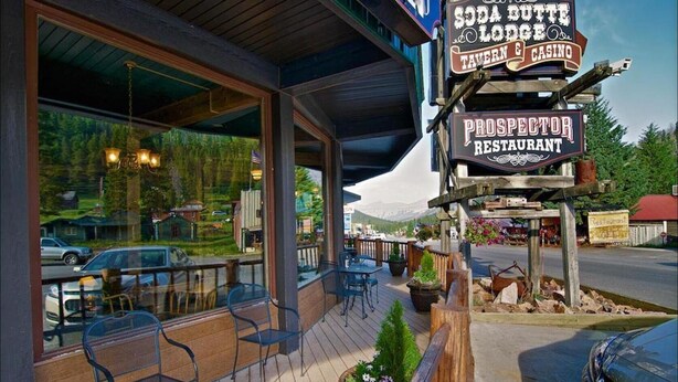 A restaurant with outdoor seating, a sign for 'Prospector Restaurant', and a view of the surrounding area. - Soda Butte Lodge (Cooke City)