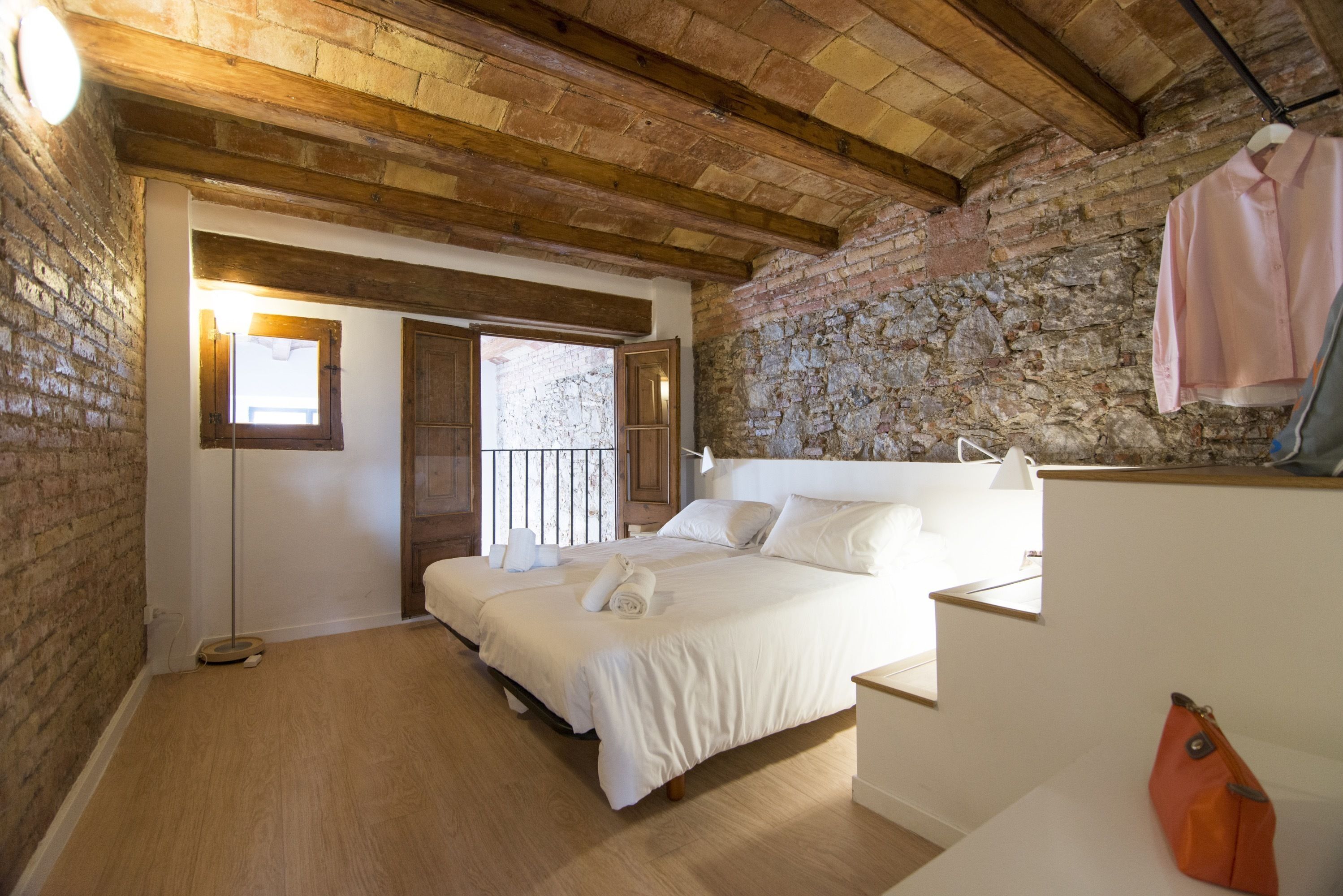 A bedroom with a large bed, wooden beams, stone walls, and a hanging garment.