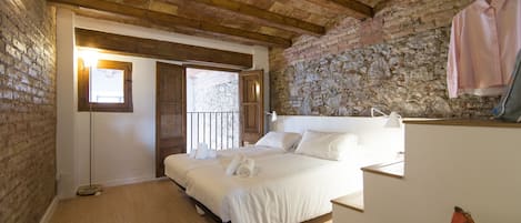Ein Schlafzimmer mit einem großen Bett, Holzbalken, Steinwänden und einer Kleiderstange.