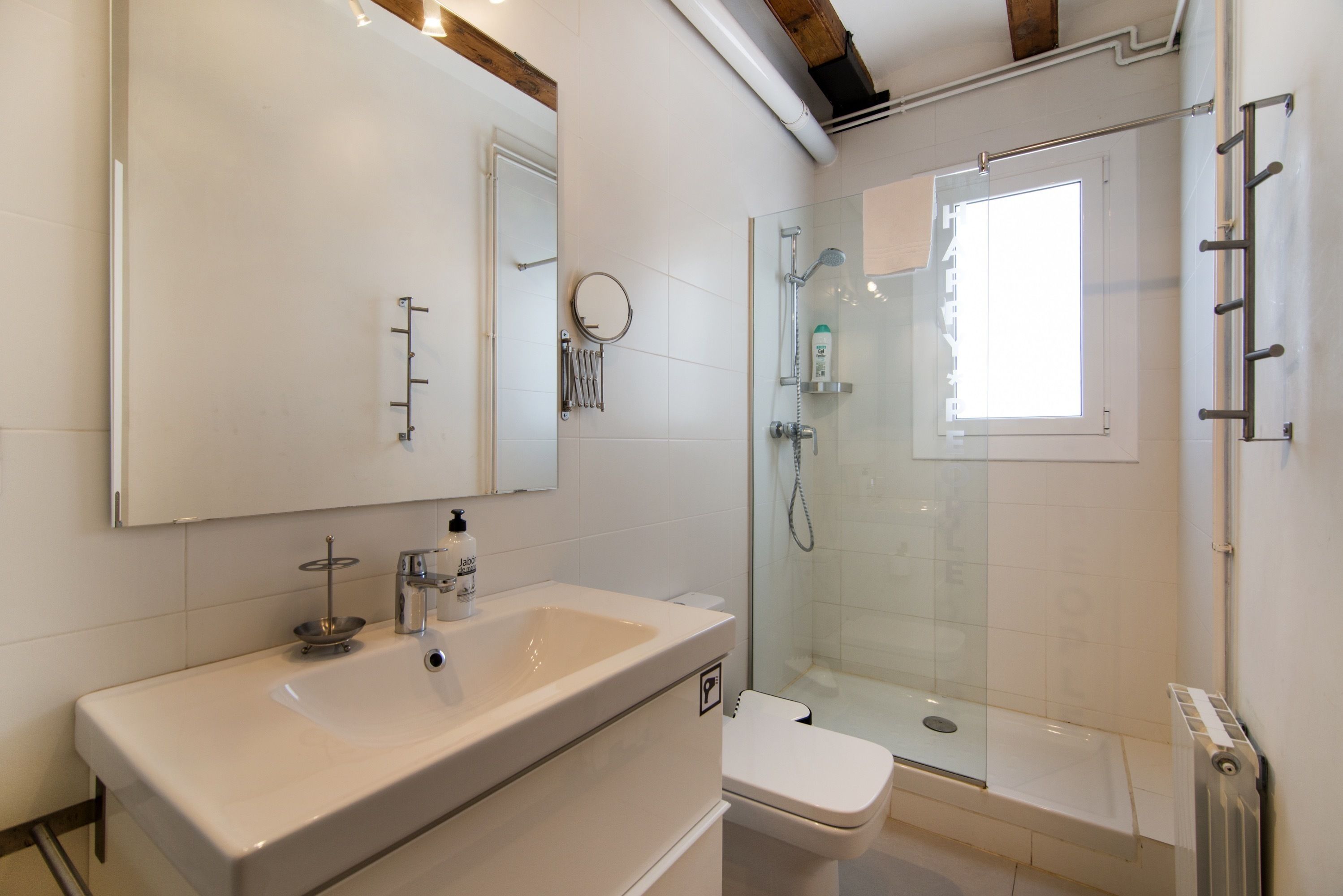 Une salle de bain moderne avec un grand miroir, un lavabo, des toilettes et une douche séparée par une paroi en verre.
