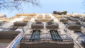 A building facade with multiple balconies, a sign reading "HAPPY PEOPLE APARTMENTS," and a yellow mailbox.