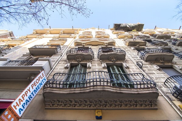 Fachada de un edificio con varios balcones, un cartel que dice "HAPPY PEOPLE APARTMENTS" y un buzón amarillo.