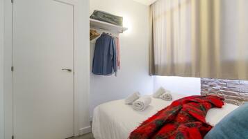 A bedroom with a bed, a wardrobe, a shelf with a blanket, and a window with curtains.
