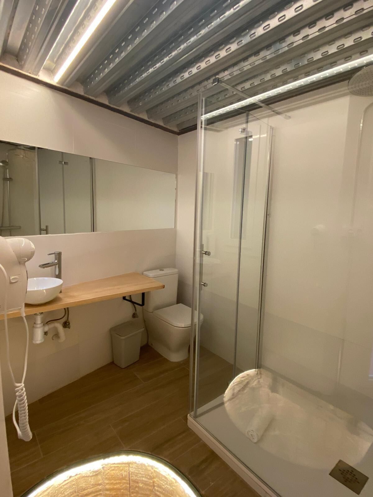 Een moderne badkamer met een douche met glazen wand, een witte wastafel en een spiegel boven de wastafel.