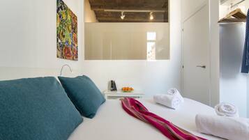 Un dormitorio con cama, almohadas, una mesita de noche con frutero, una toalla y un perchero.