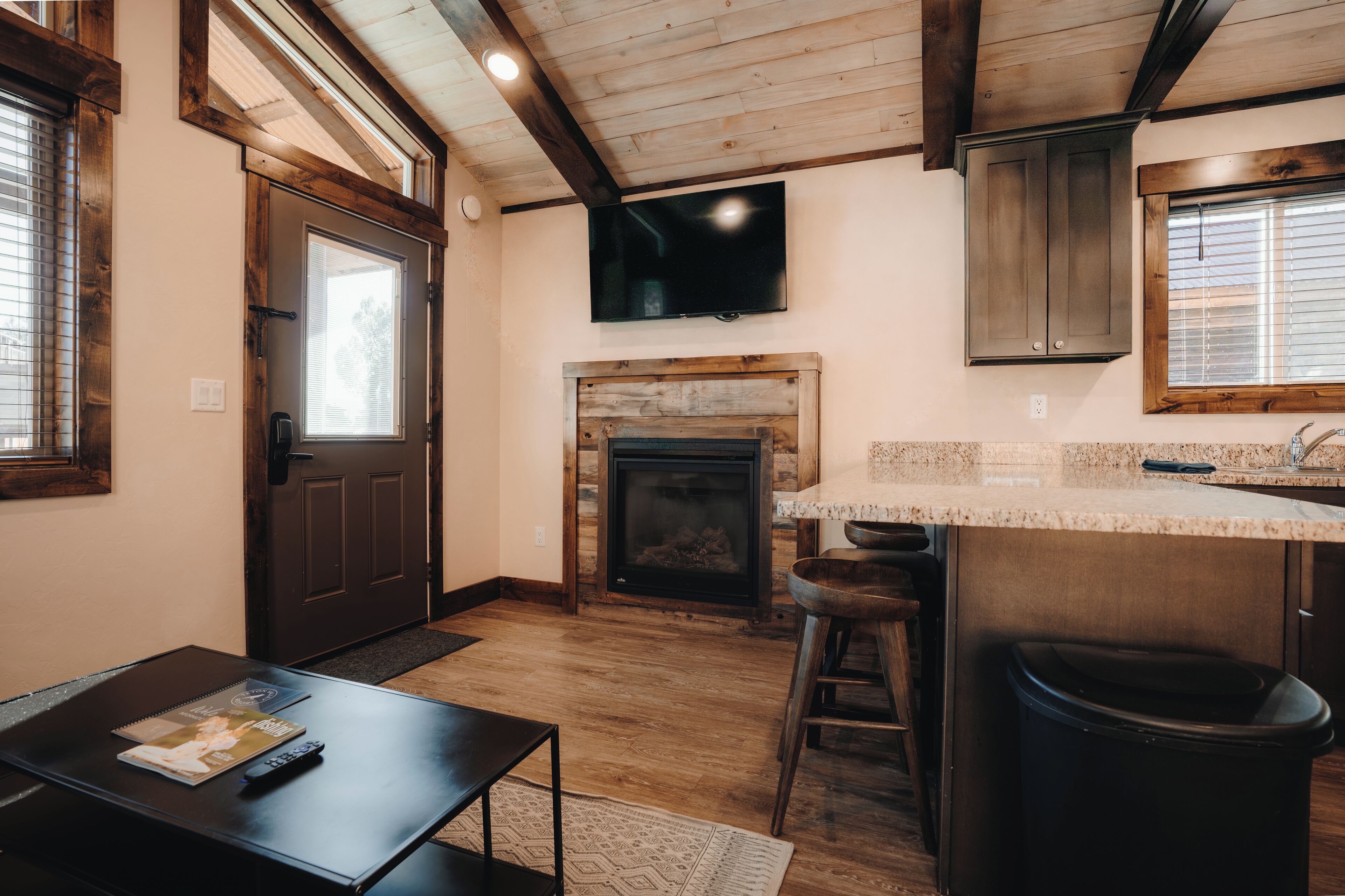A cozy kitchen with a fireplace, wooden beams, a TV, and a bar area.