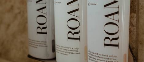Three bottles of ROAM shower gel on a metal shelf against a tiled wall.