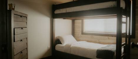 Une chambre avec un lit superposé, une commode en bois et une fenêtre.