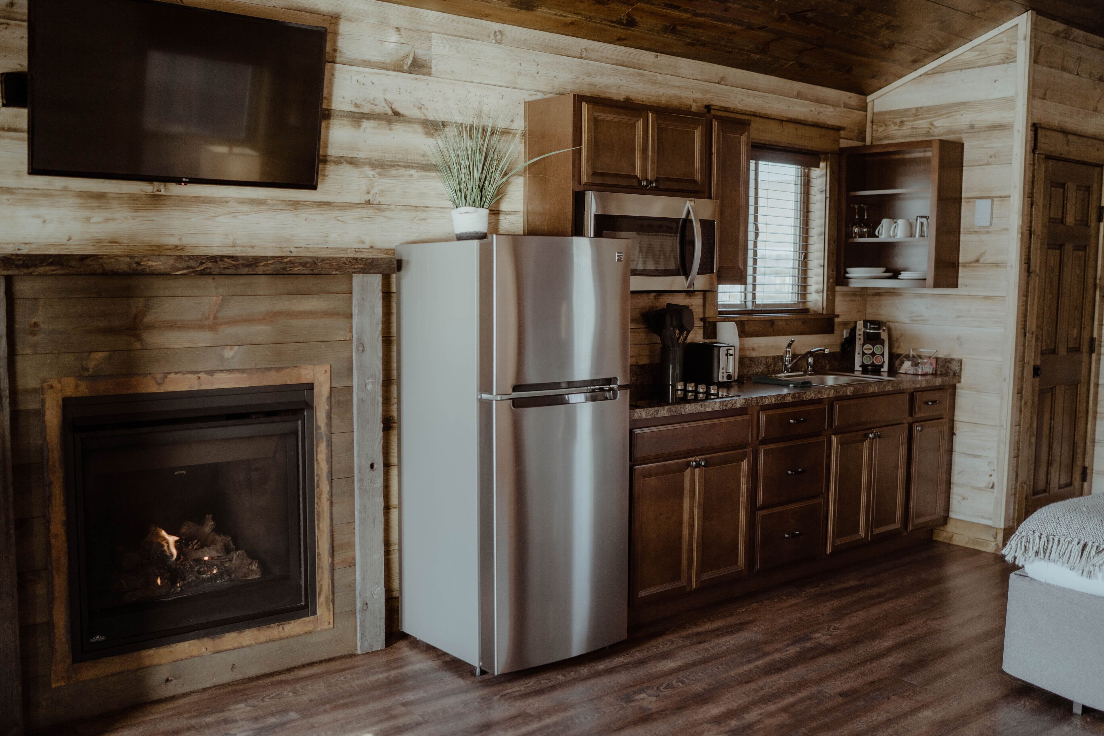 Cocina de cabaña de madera con refrigerador de acero inoxidable, armarios de madera, microondas y chimenea.