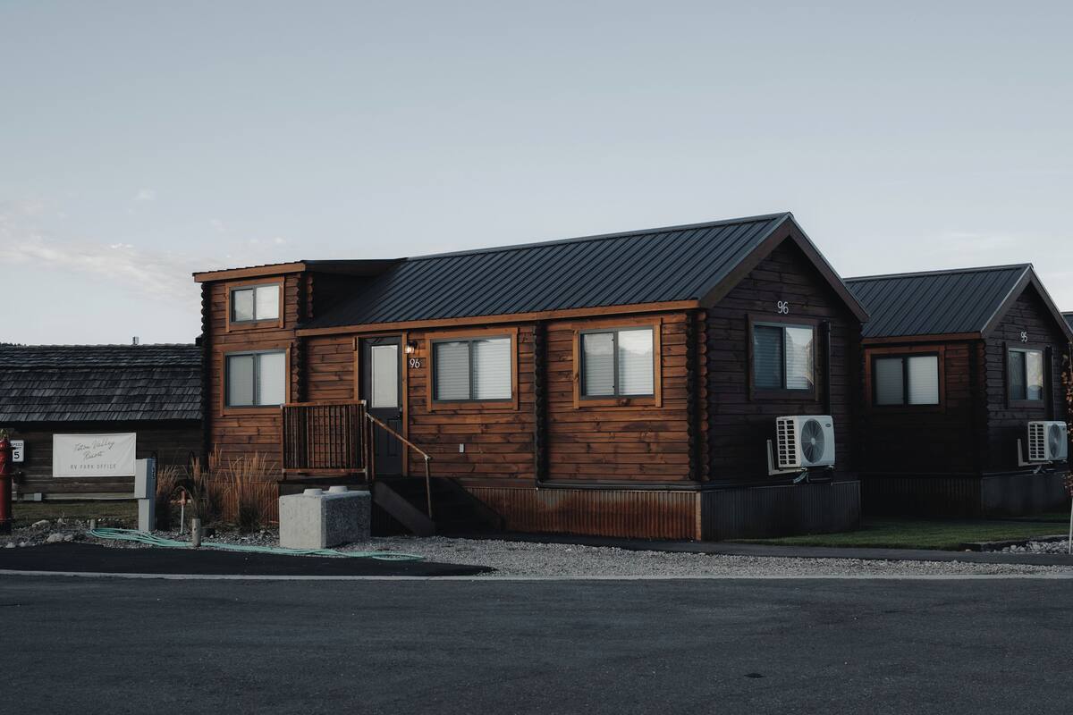 A two-story wooden cabin with a metal roof, a small porch, and an air conditioning unit.