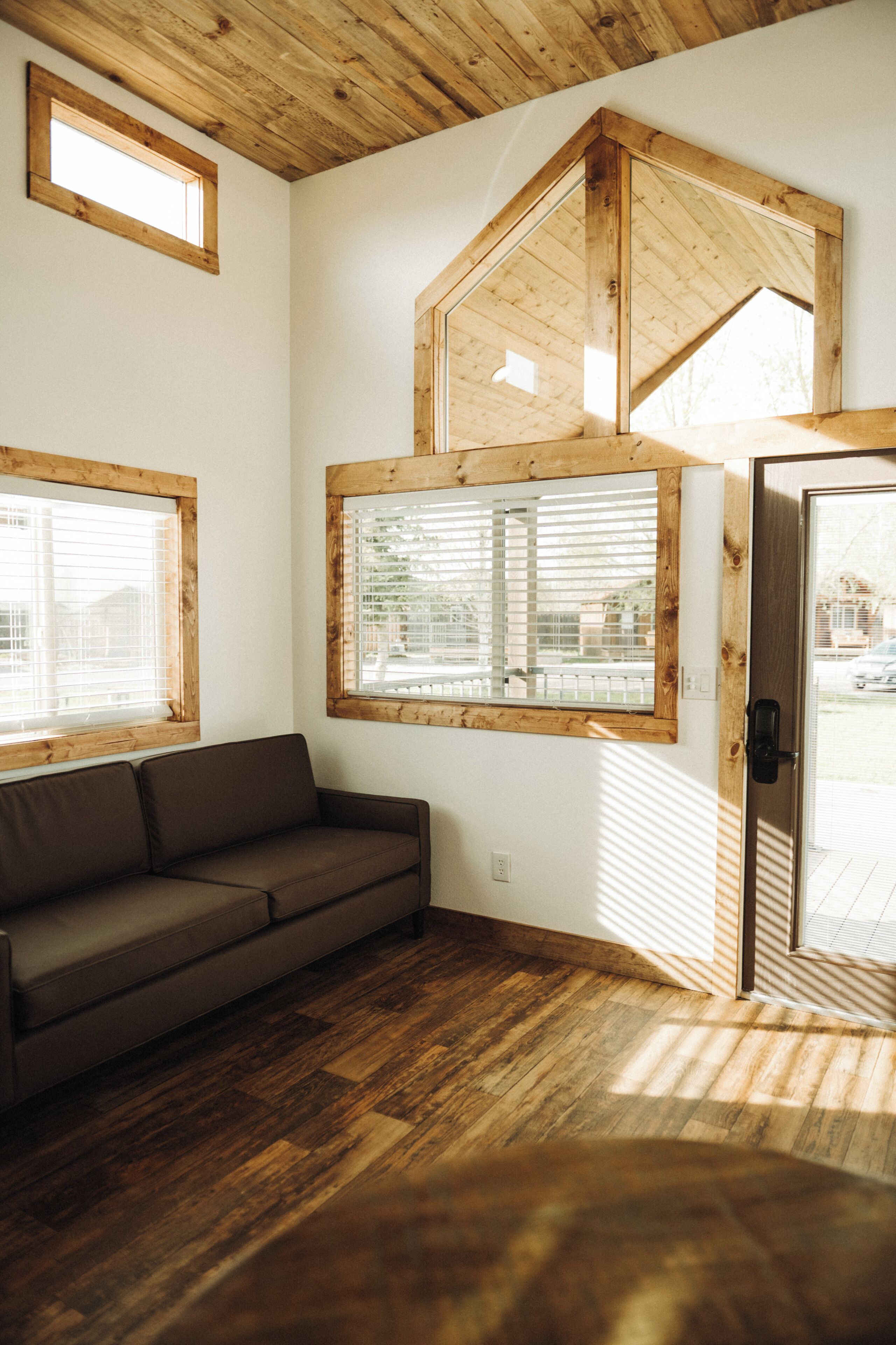 Une pièce avec un plafond en bois, un canapé marron et de grandes fenêtres à cadre en bois.