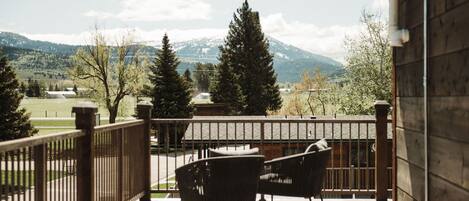 A wooden deck with two chairs and a table, overlooking a mountainous landscape.